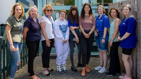 The current team at Springboard are all standing together outside of the building. There are nine women in the picture smiling at the camera on a sunny day.