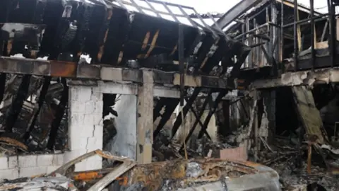 The burnt out shell of the workshop building showing charred remains and no roof