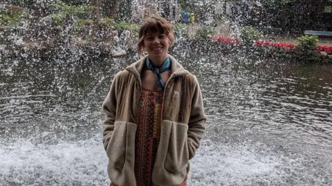 Gina Shutler A woman stands in front of a fountain, smiling at the camera.