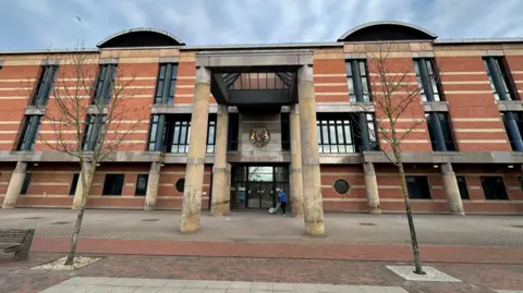 Teesside Crown Court. A large three storey building made from red brick with long narrow black windows. Four large round yellow stone columns support a pyramid shaped glass roof above the front door.