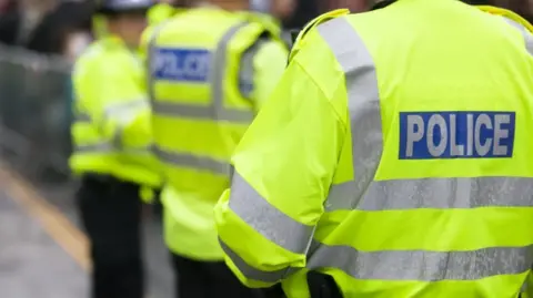 A generic image of three police officers wearing yellow police jackets. Their faces are not shown.