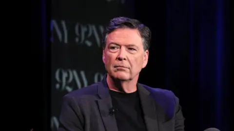 Former FBI director James Comey wearing a dark suit, with a dark background