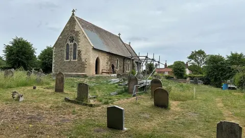 The South Wolds Partnership The newly repaired church seen from the graveyard. It has new light-coloured stone work with a new doorway and scaffolding nearby 