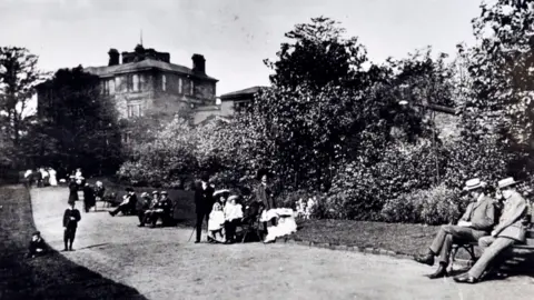 Salford Local History Library Black and white photograph of Buile Hill Mansion with people gathered on the lawns and trees surrounding mansion