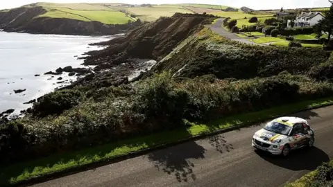 BRC A rally car takes part in a previous event on the island, seen driving on a road near cliffs and sea