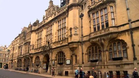 Oxford Town Hall looks grand from the street, as people walk past.