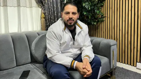 Syrian refugee Ali Abi Zaid who lives in Cheltenham poses for a photo on a grey sofa