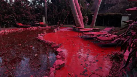 Getty Images Fire retardant covers a excavation  and lounge chairs aft  being dropped from a firefighting craft  battling the Palisades Fire.