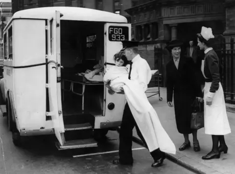 Hulton Archive via Getty Images A black and white photo showing 10-year-old Eileen Clifton being transferred from University College Hospital to an ambulance which is to take her to another hospital during an evacuation of patients after the discovery of an unexploded bomb near the building