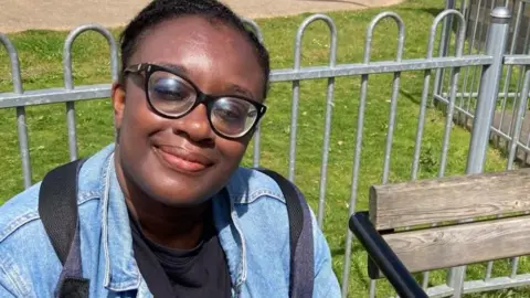 Brian Farmer/BBC Catherine Yeboah in blue jacket sitting on park seat