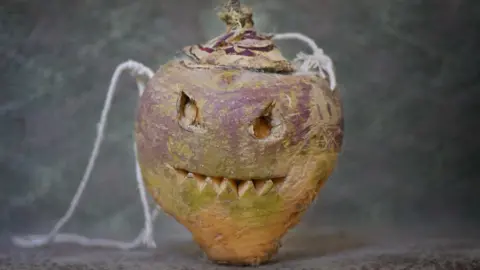 Culture Vannin A turnip carved with a spooky face carved in the style of a pumpkin, with string attached for carrying. 