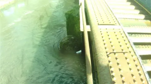 A high water level next to a railway track. There is a white marker on the bridge and the water is above it. 