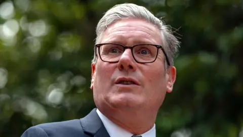 Sir Keir Starmer is pictured in a close-up with a backdrop of trees blurred out.