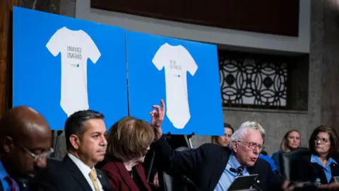 Getty Images Senator Bernie Sanders holding up   images of babe  onesies that work   'Unvaccinated. Unafraid'. 