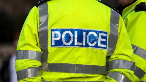 A police officer's high-vis coat in yellow, as seen from the back, bearing the word "police".