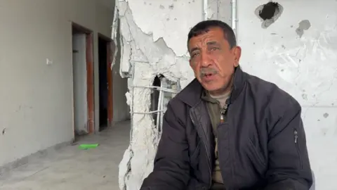 Marwan sits in front of a devastating wall inside the building corridor