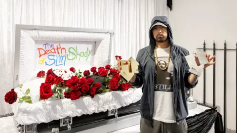 The Official Charts Company  Eminem standing in front of a white coffin, holding two charts awards 