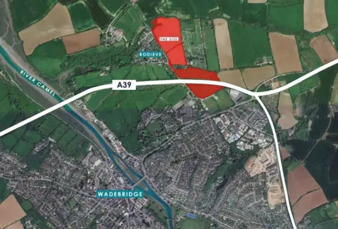 An aerial birds' eye map view of the town of Wadebridge and the surrounding areas. The proposed site is marked out in bright red while the main road is marked in white.  