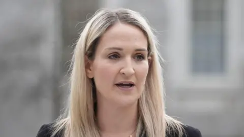 Helen McEntee, who has long blonde hair and is wearing a black jacket and gold necklace