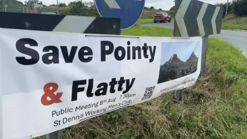 A sign reading "save pointy and flatty" put up on a roundabout. The sign features an image of the clay waste tips