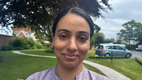 An Asian woman with a purple top smiling at the camera