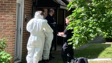 Forensic officers and police officers stood outside of a brick property.