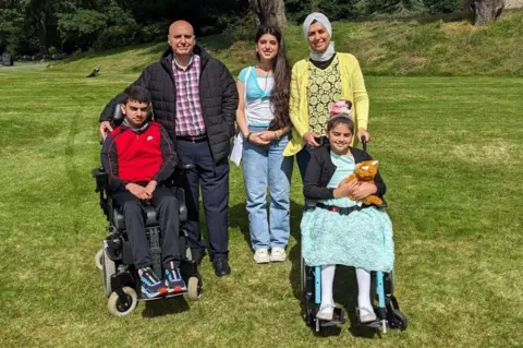 CHAS A husband and wife, with a young woman and two children in wheelchairs pose for the camera outside
