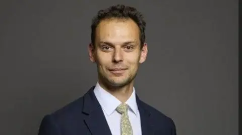 PA Media Josh Simons has dark hair, a pale green tie, white shirt and blue suit