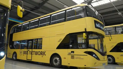 PA Media A line of three parked yellow buses in a manufacturing depot