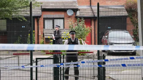 PA Media Police standing at cordon around house subject to a police search