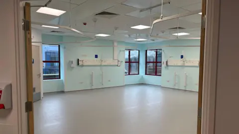 A clean light blue and white hospital ward with lost of natural light from the windows.