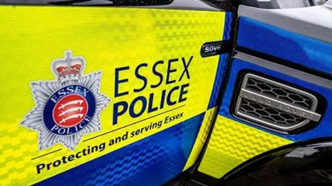 A car with "Essex Police protecting and Serving Essex" written on the side. The police badge with blue and yellow colours can also be seen.