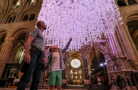 Durham Cathedral A boy points up at the thousands of white paper doves hung inside the cathedral as he stands with his father.