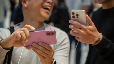 Getty image customers hold Apple iPhone 16 and 16 Pro in a shop