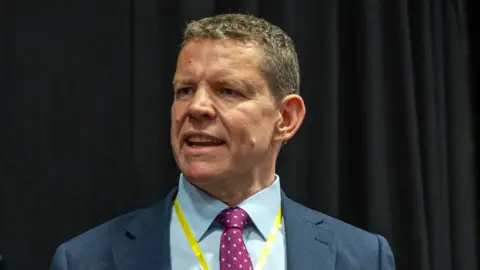 Rhun ap Iorwerth, a man with short brown hair in a blue suit