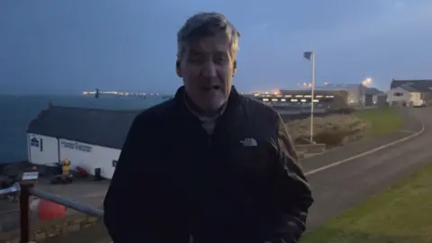 Rob Thomas stands on the seafront looking into the camera