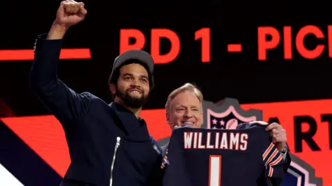 Caleb Williams clenches his fist and smiles towards the crowd while posing with a Chicago Bears jersey