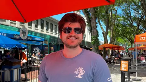 A young man with brown hair wearing sun glasses and a blue t-shirt