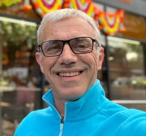 Mark Krantz A man wearing black-framed glasses and a bright turquoise fleece is smiling at the camera.