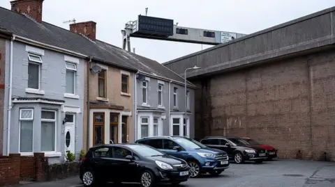 Getty Images Cars parked outside houses in a cul-de-sac street in front of a large concrete wall which holds up the M4 motorway at Port Talbot