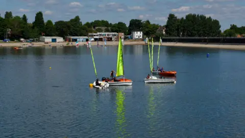 Four sailing dinghys on a reservoir. The vessels have lime green sails.