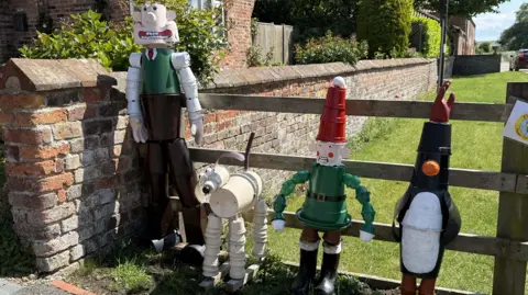 BBC/Amber Gash Four flowerpot statues depicting characters from BBC series Wallace and Gromit stand in front of a wooden gate.