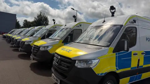 Nine police vans lined up with cameras attached to the top