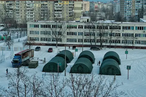 Getty Images Two rows of rigid tents, six in total, in a public space in Kyiv. There is snow all around and modern buildings in the background.