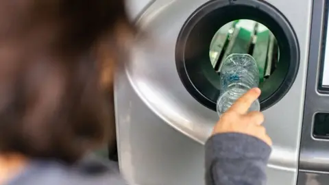 Getty Images A woman puts a plastic bottle into a reverse vending machine