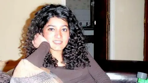 Aleena family Zara Aleena, dressed casually with long curly hair spilling over her shoulders. She is sitting on a sofa and looks at the camera, seemingly mid-comment. She looks cheerful and engaged with the cameraperson.