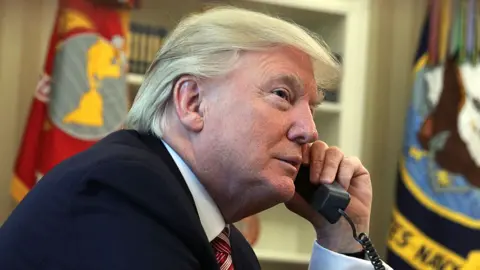 Donald Trump holds a landline phone to his ear in the Oval Office