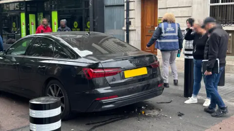 The back of a car hit by a rising bollard, with debris left on the road.