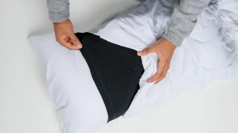 IAN REYNOLDS - NOTTINGHAM TRENT UNIVERSITY White pillow with black sleeve in the middle, as a pillow case is pulled over. 