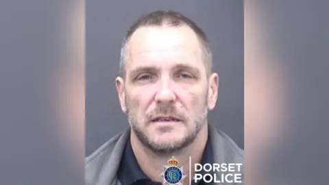 A mugshot of a man with Dorset Police's logo in the bottom right corner